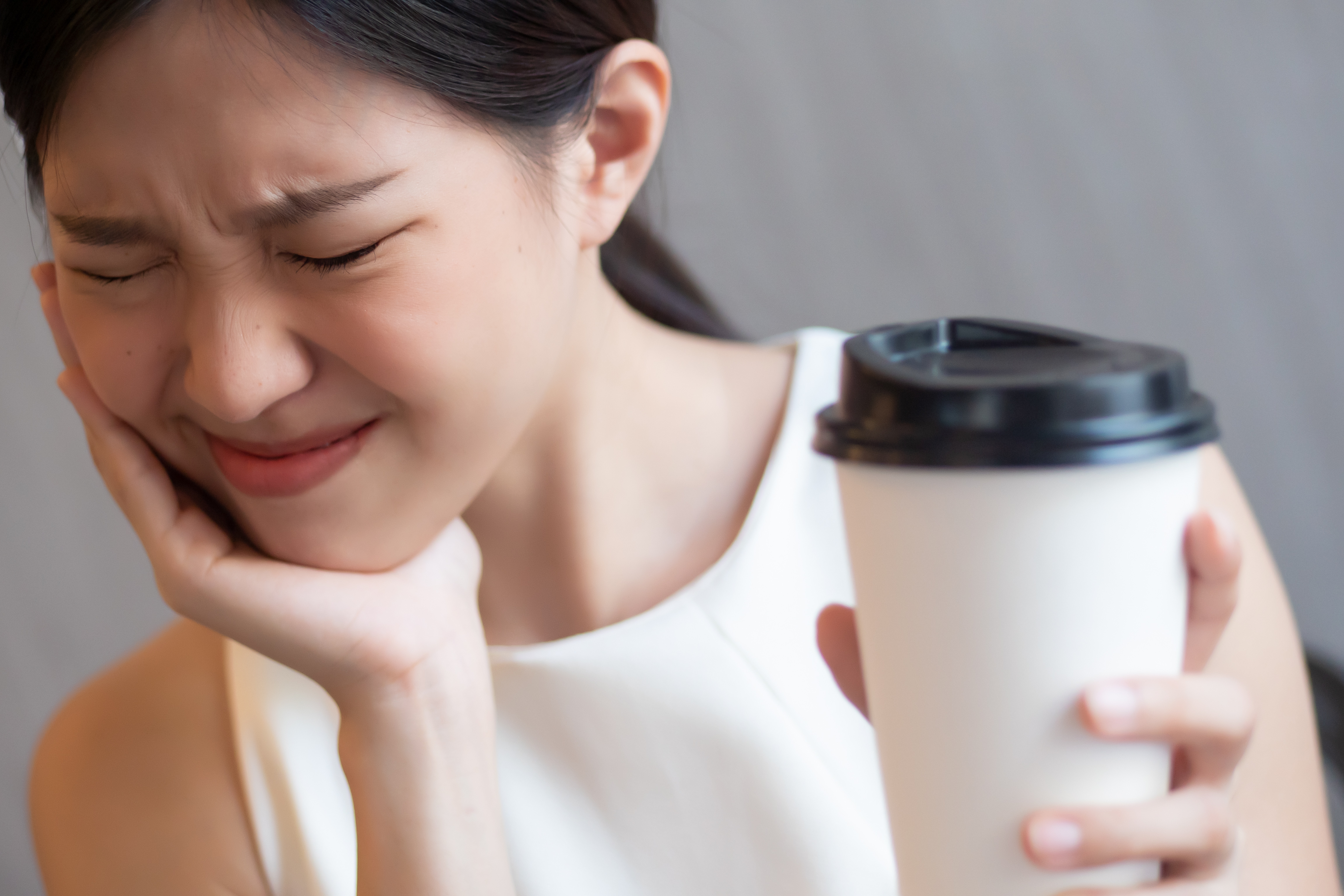 Asian woman holding a coffee cup has pain from a broken tooth.