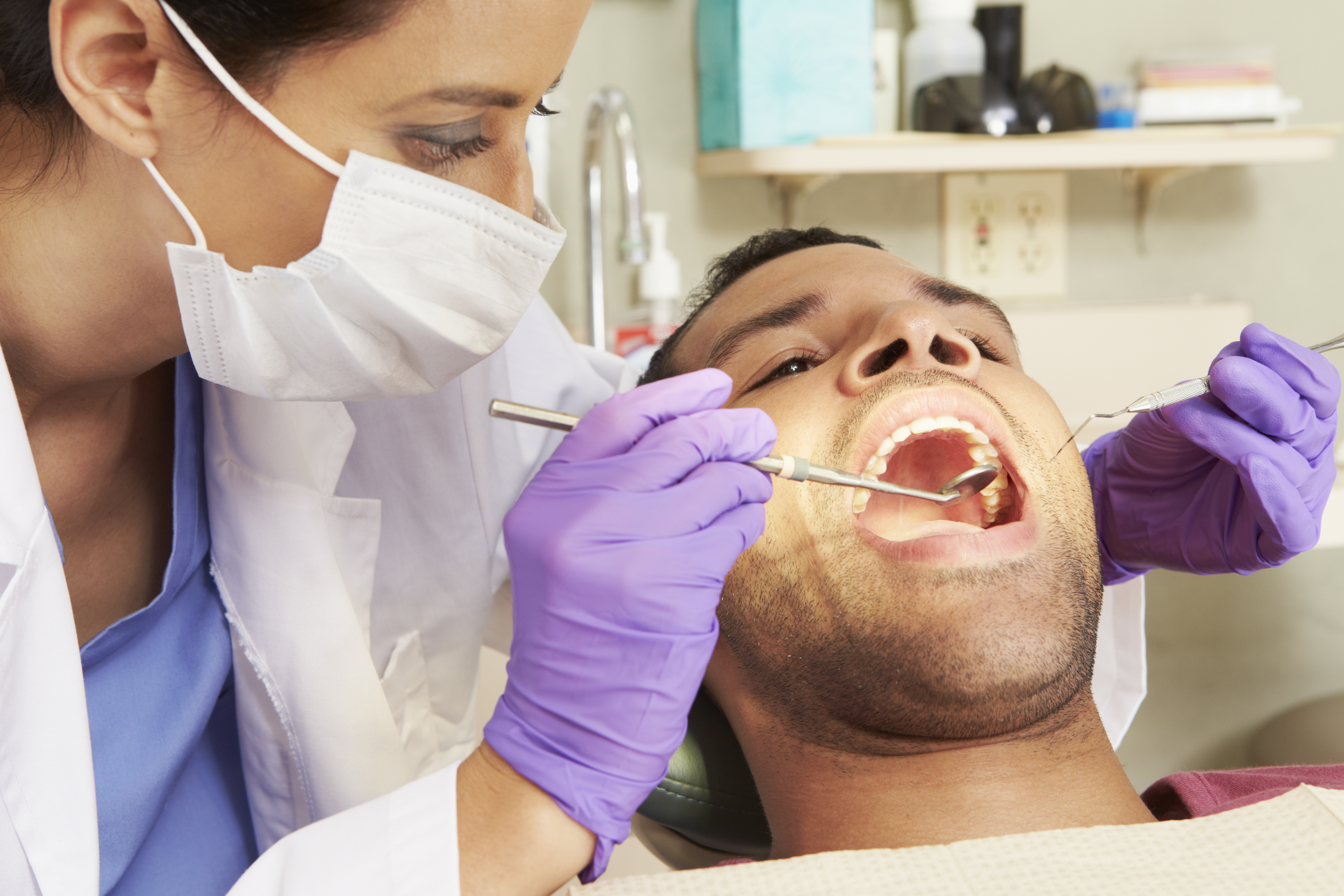 A female dentist weaning a face mask and gloves examines a patient’s broken tooth.