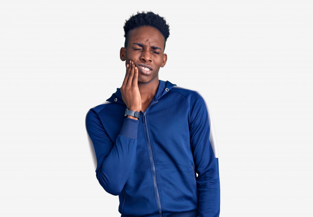 A young black man in a blue zip-up jacket holds his tooth in pain from a possible broken molar.