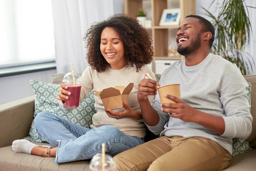 Happy Black couple enjoy takeout and drink a berry smoothie with a straw to help keep their teeth white.