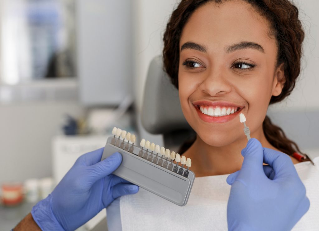  Dentist shows a smiling Black patient the possible results of a teeth whitening treatment.