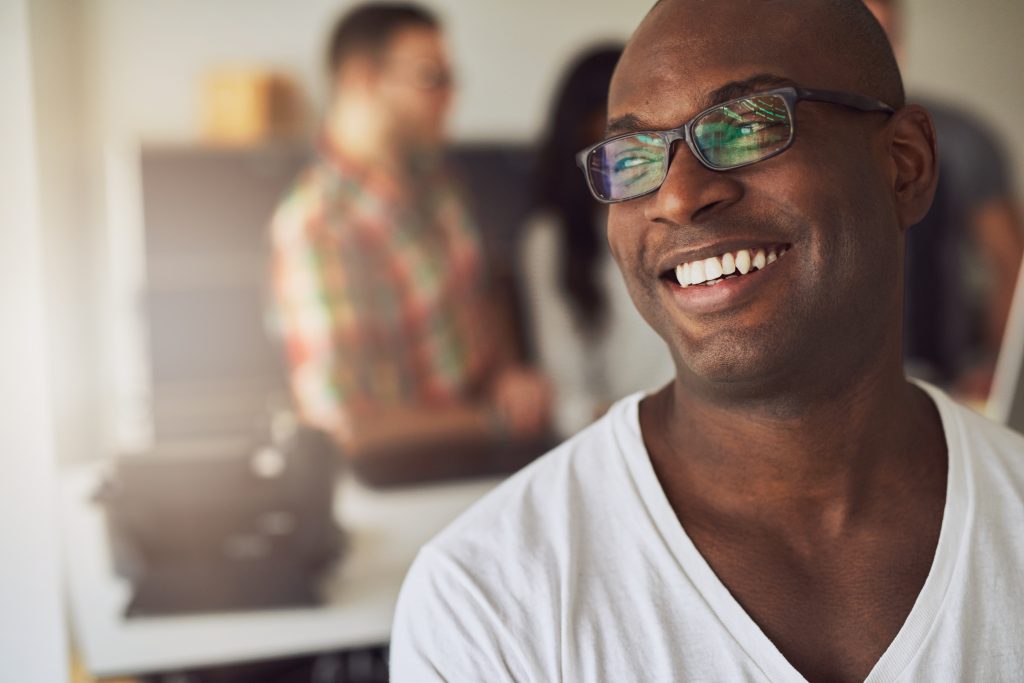 Handsome Black man in white T-shirt smiles with bright, white, straight teeth.