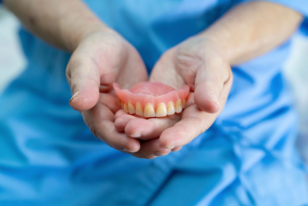 Prosthodontist wearing scrubs holds fixed upper denture in his cupped hands, illustrating denture repair.
