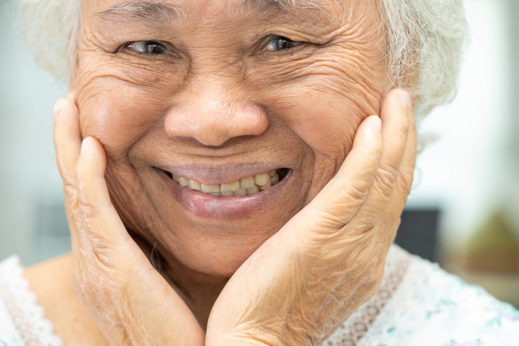 Senior woman holds hands to cheeks and smiles, wearing dentures repaired at Penn Dental lab in Philadelphia, Pennsylvania.