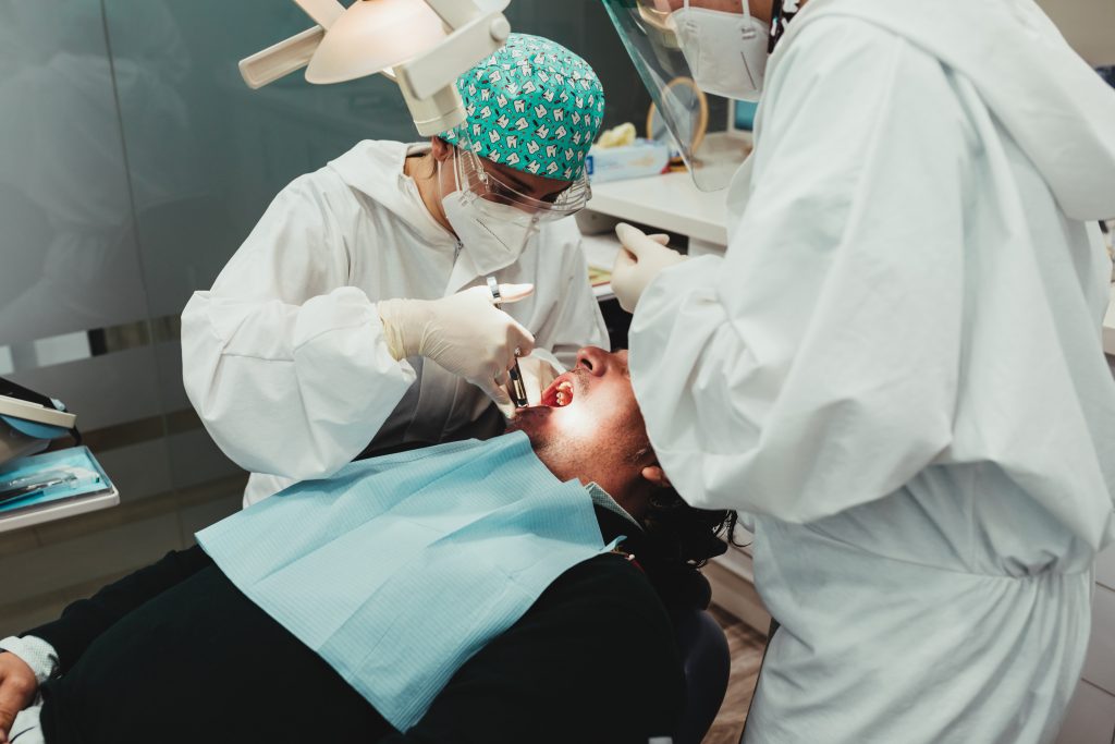 Two dental specialists in personal protective equipment provide root canal treatment for a male patient. 