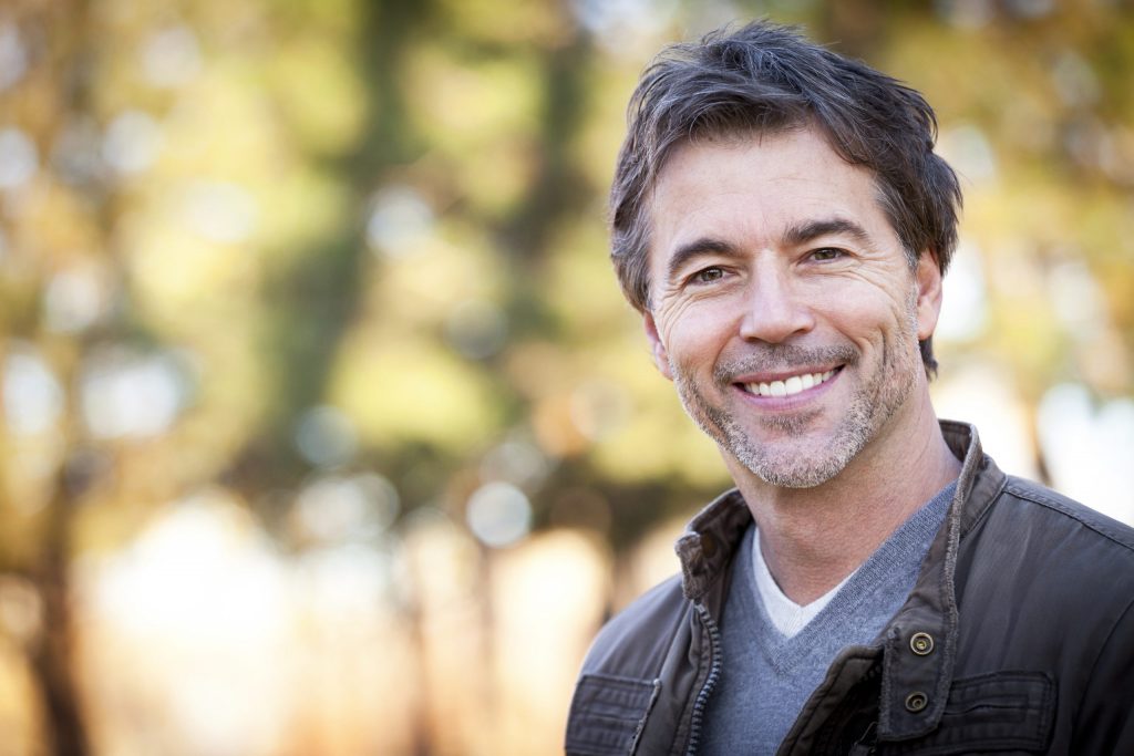 A man smiles with straight white teeth outside after visiting the prosthodontist. 