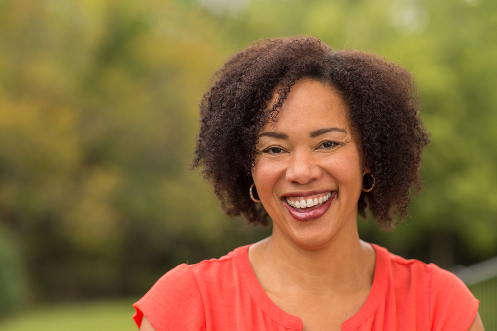 A young woman smiles outside after she’s gone through the dental implant process. 