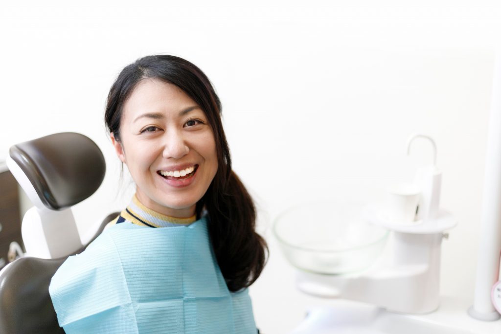 An Asian woman wearing blue dental blue bib smiles at the dental office.