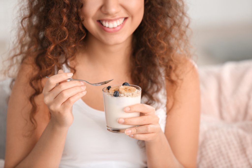 Smiling young Black woman enjoys a snack of yogurt and berries.