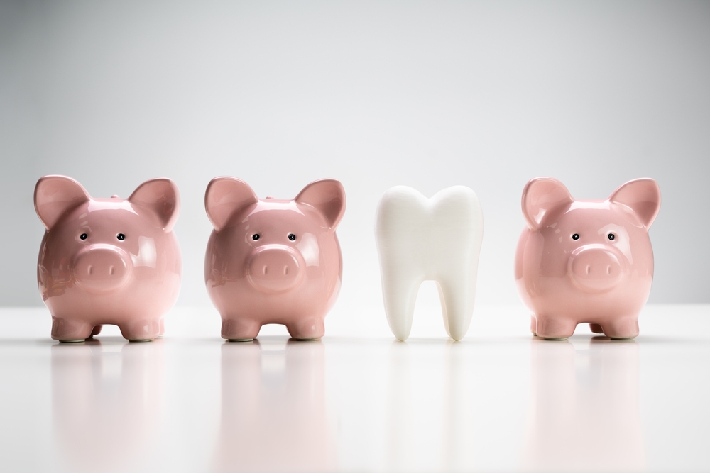  A plastic tooth is in a row with three pink piggy banks to suggest the benefits of brushing teeth can save money.