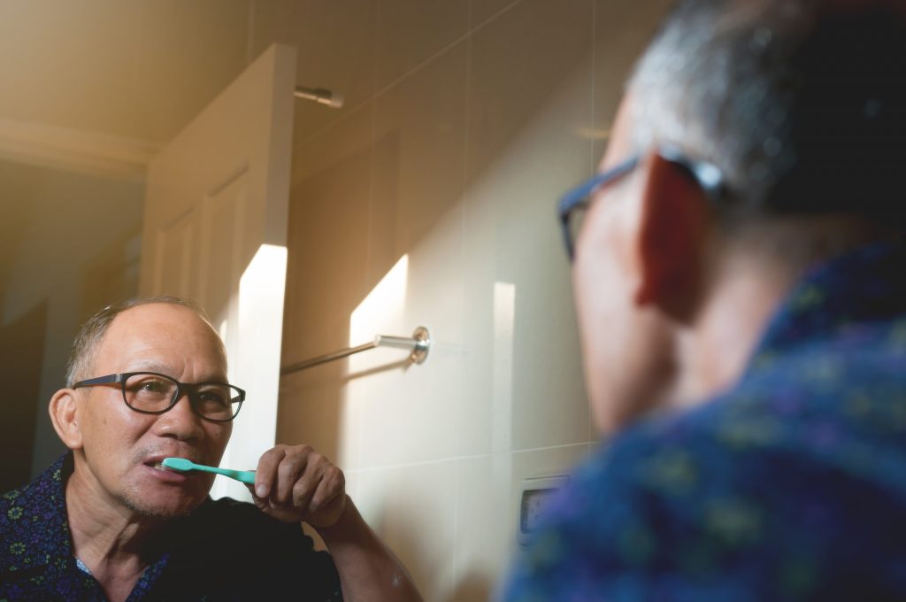  Mature Asian male wearing black glasses brushes his teeth with a blue-green toothbrush. 