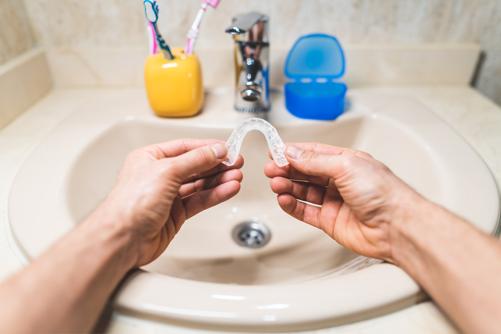 A person cleaners their invisible aligners over a sink.