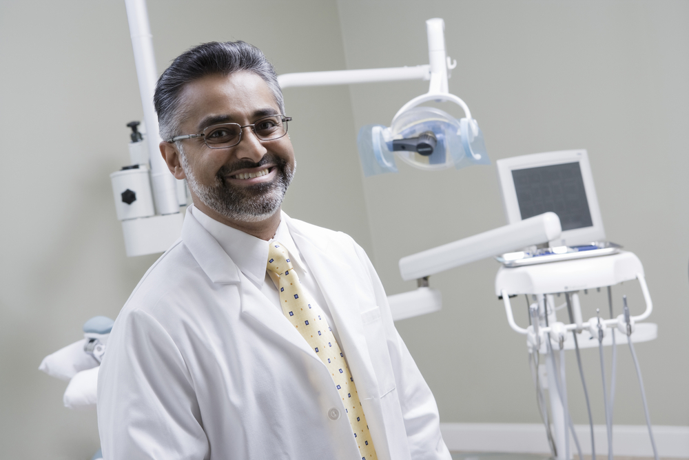  Professor in dental jacket smiles as he poses for a picture in an examination room at dental faculty practice.