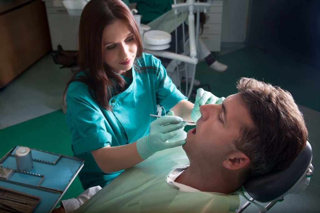 Dentist uses tool to sculpt tooth-colored resin in mouth of man reclining in dental chair during chipped tooth bonding.