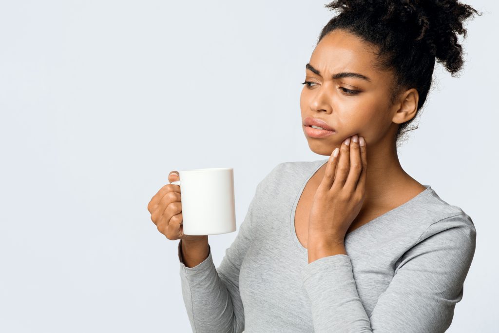 Young Black woman has tooth sensitivity while drinking hot coffee which could be a sign of receding gums. 