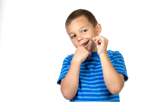 Brown-haired boy with blue striped shirt flossing teeth against a white background.