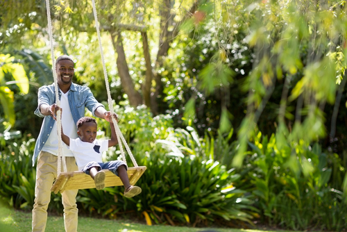 Happy man pushing his son in a swing at the park.