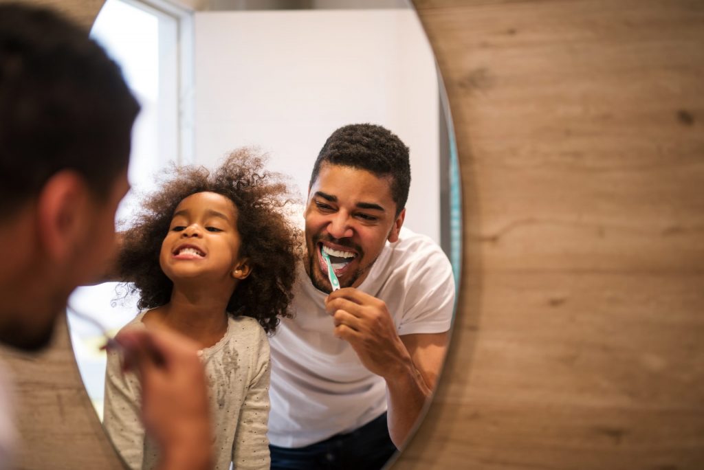 Smiling father and daughter brushing their teeth at home.