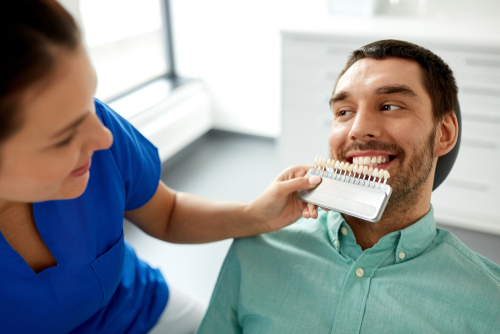 A family cosmetic dentist helps a hispanic man in a green shirt match his natural tooth color for veneers.