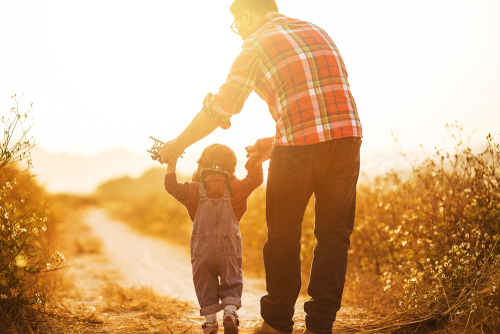 Father helps his toddler walk on a sunny day.