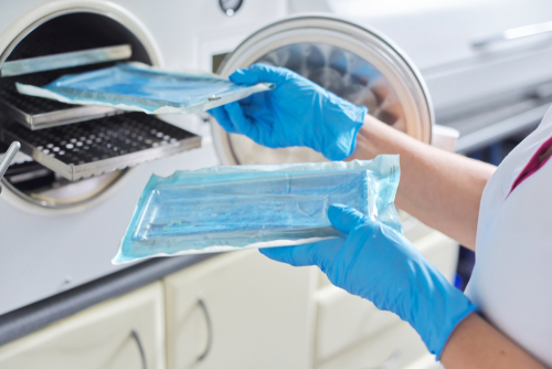 Woman wearing gloves places dental instruments in autoclave sterilization.