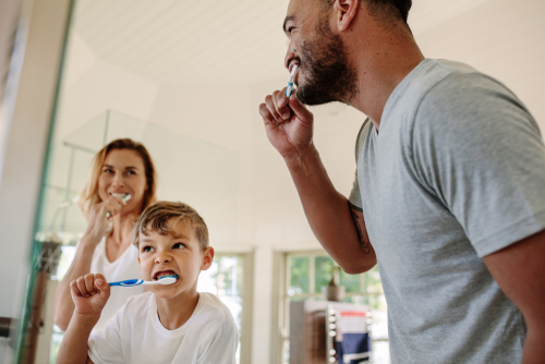 Boy brushes teeth, accompanied by his father and mother.