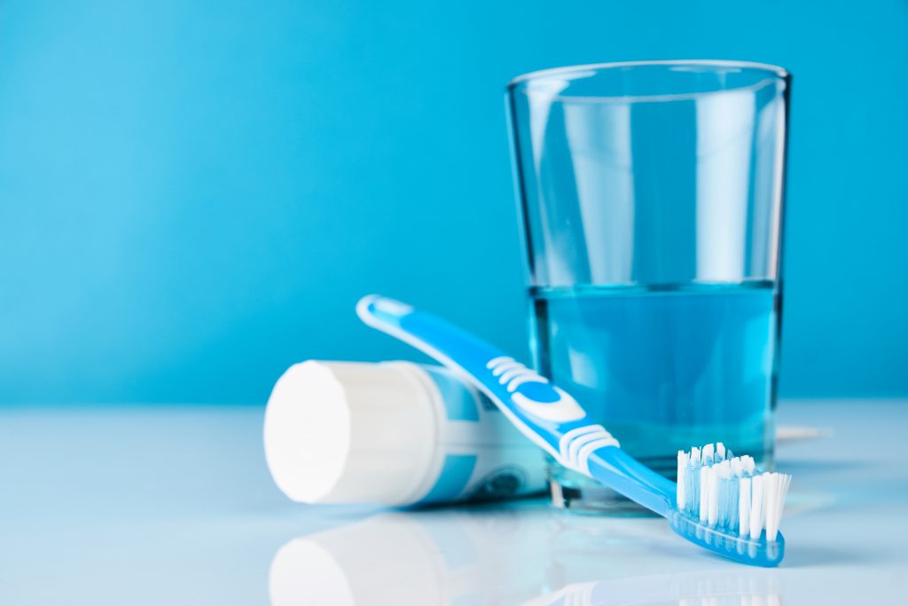 Blue background with toothbrush, toothpaste, and a glass of water.