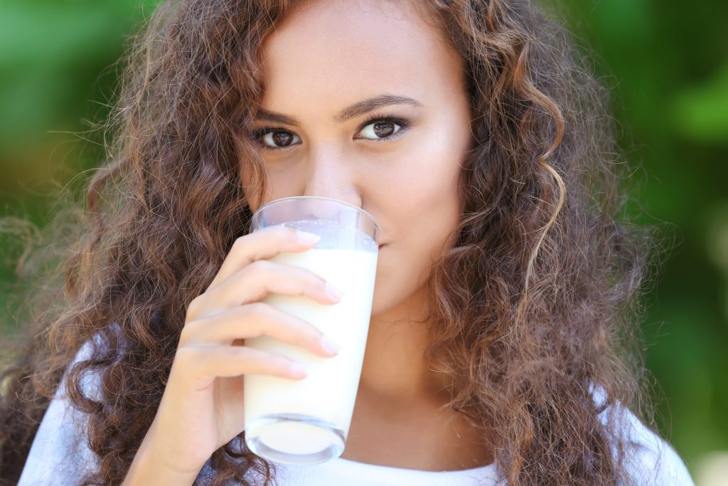 A young woman drinks a glass of milk outside to help prevent tooth enamel erosion. 