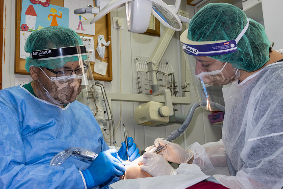 Two dentists wearing facemasks and personal protective equipment (PPE) perform oral surgery on a patient. 