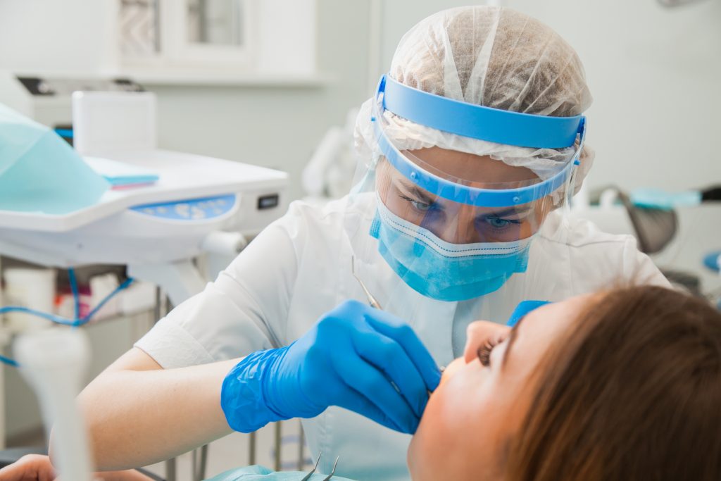  Dentist wearing face shield, mask, and gloves performs endodontic surgery to treat a woman’s dental abscess.