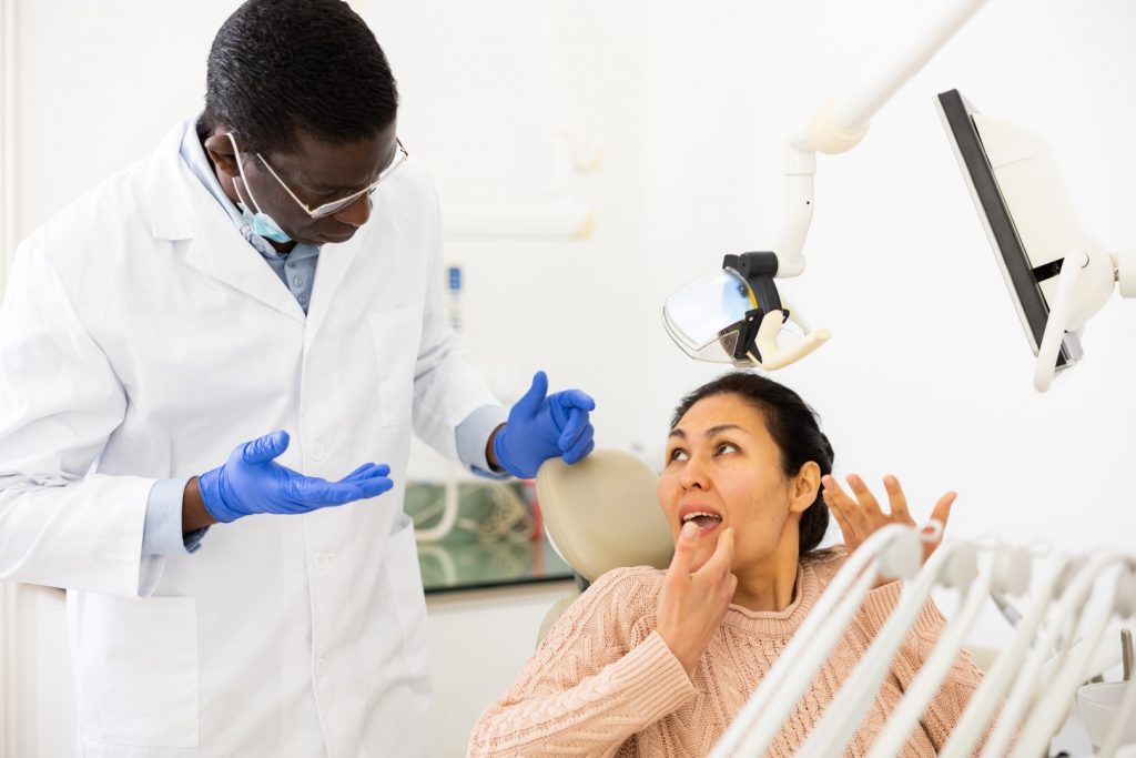 A woman in a dental chair points to where she saw a black spot on her tooth while talking to her dentist.