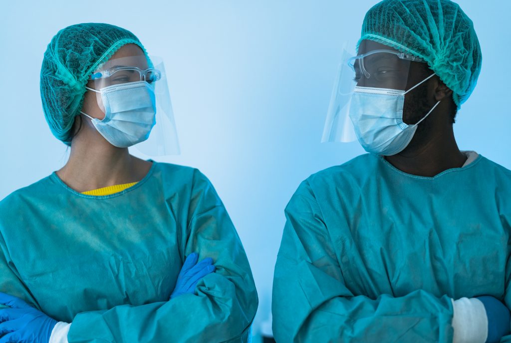 Female and male dentists side by side wearing blue/green full personal protective equipment (PPE.)