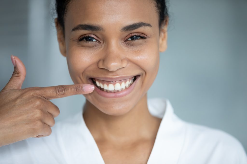 Black teen girl points to her healthy, bright smile after having her braces removed. 