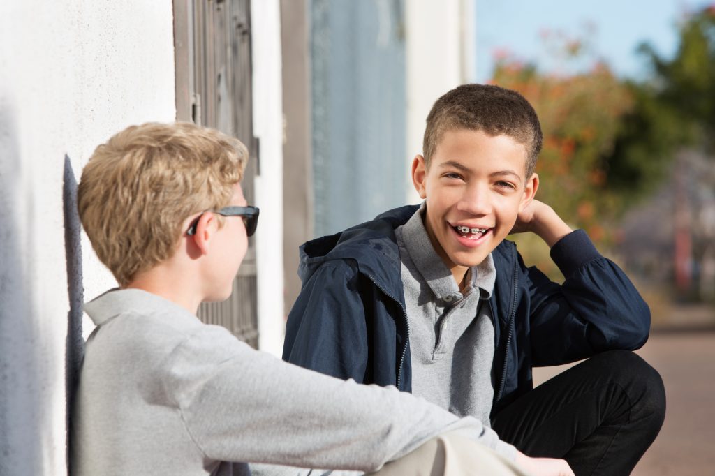 Young boy with braces on his teeth smiles while talking to a friend. 