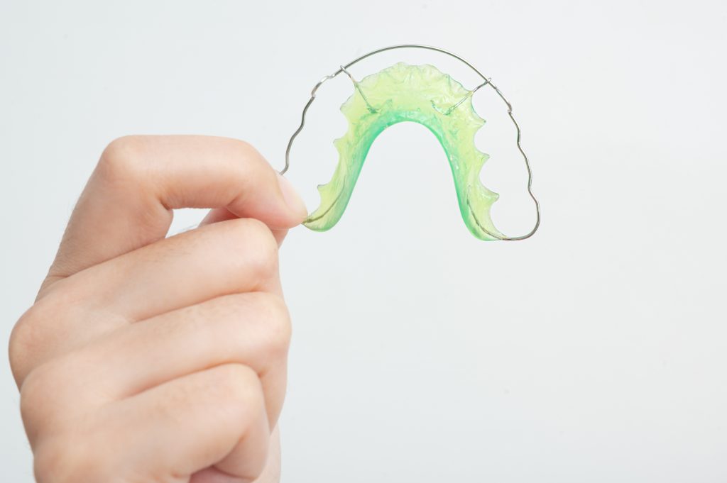 man’s hand holds a green dental retainer.