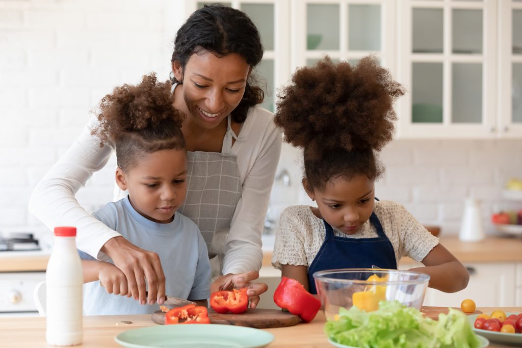 A Black mother and her two daughters make a healthy snack in the kitchen.