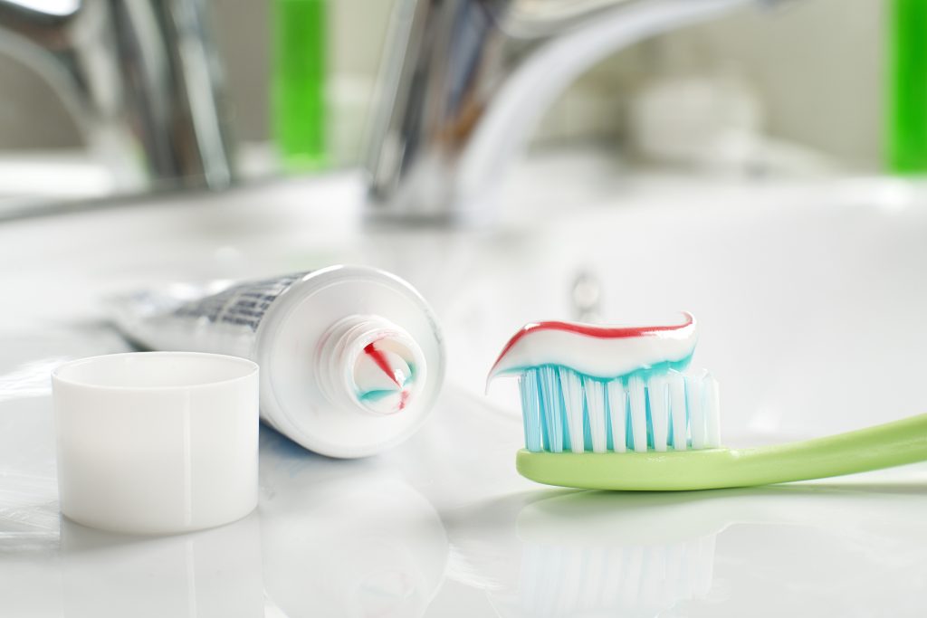 A closeup of fluoride toothpaste on a toothbrush next to a bathroom sink.