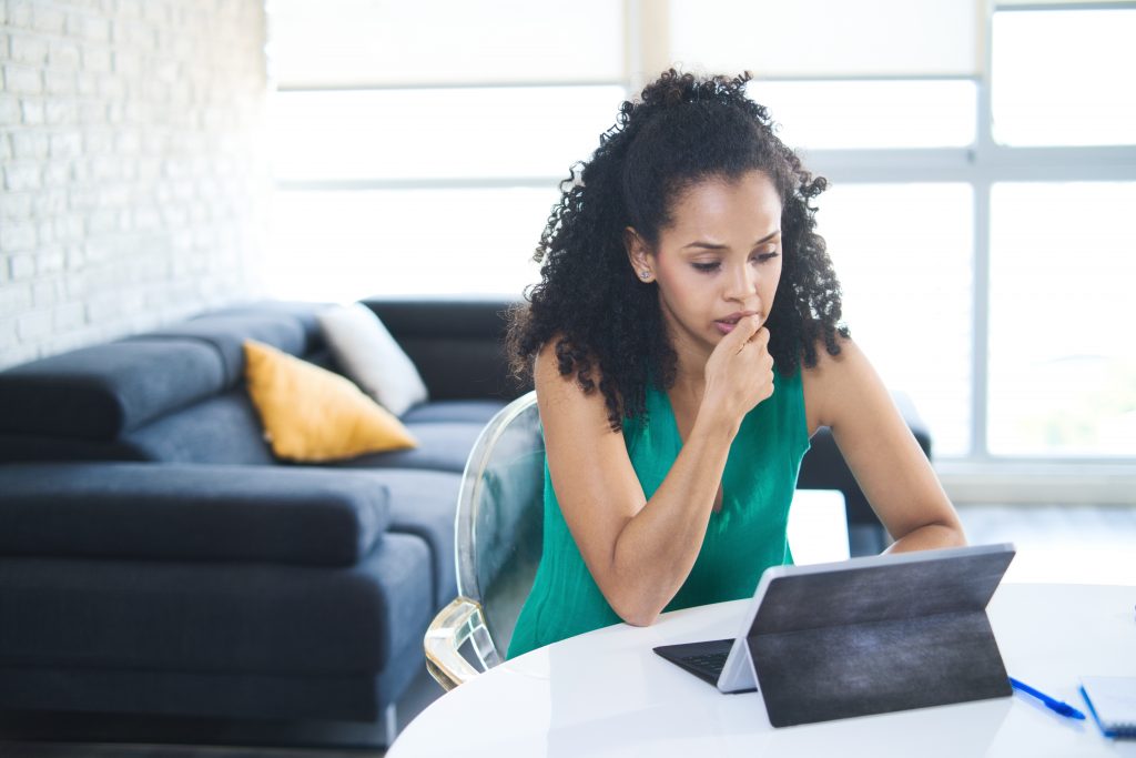 Nervous or stressed Black woman chews her fingernail while looking at a laptop computer.