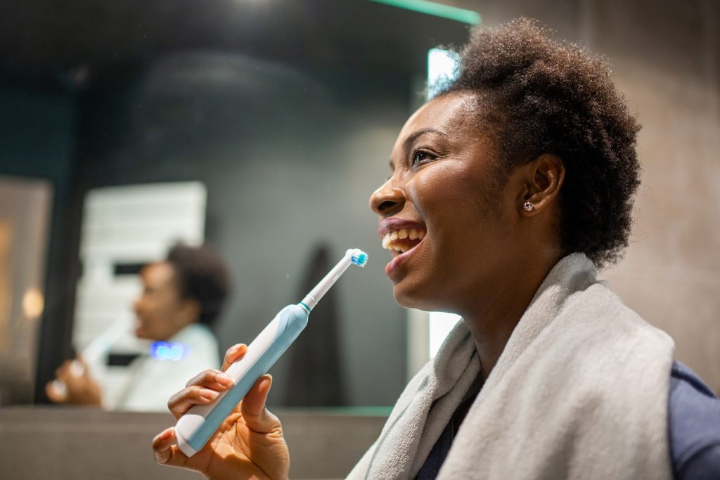 A woman uses an electric toothbrush with fluoride toothpaste on its bristles to brush her teeth, a natural teeth whitening method. 