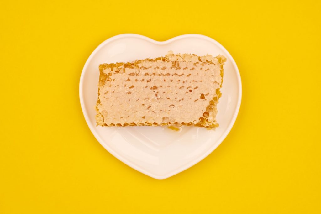 A piece of honeycomb is on a heart-shaped plate on a yellow background. 