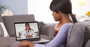Young Black woman touches her jaw while speaking to her oncologist via a computer. 