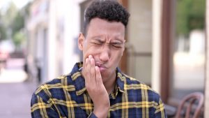 Young man in a plaid shirt has severe tooth pain and touches his face. 