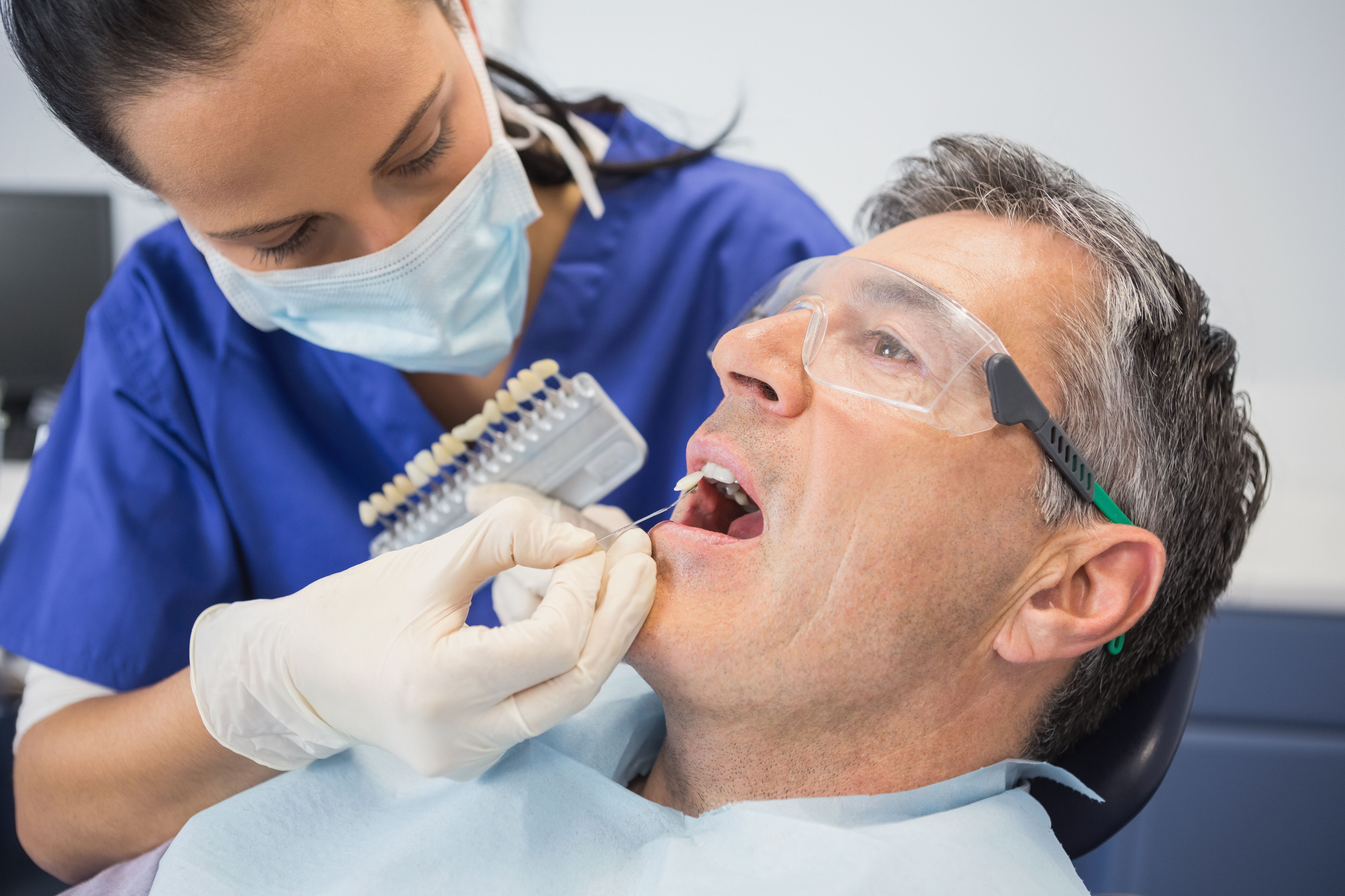 Philadelphia dentist performs cosmetic dental surgery, placing implants in mouth of patient in dentist’s office chair.
