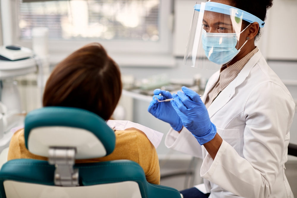 A dentist wearing a mask, face shield, and gloves is ready to help a patient who has several teeth hurting at once.