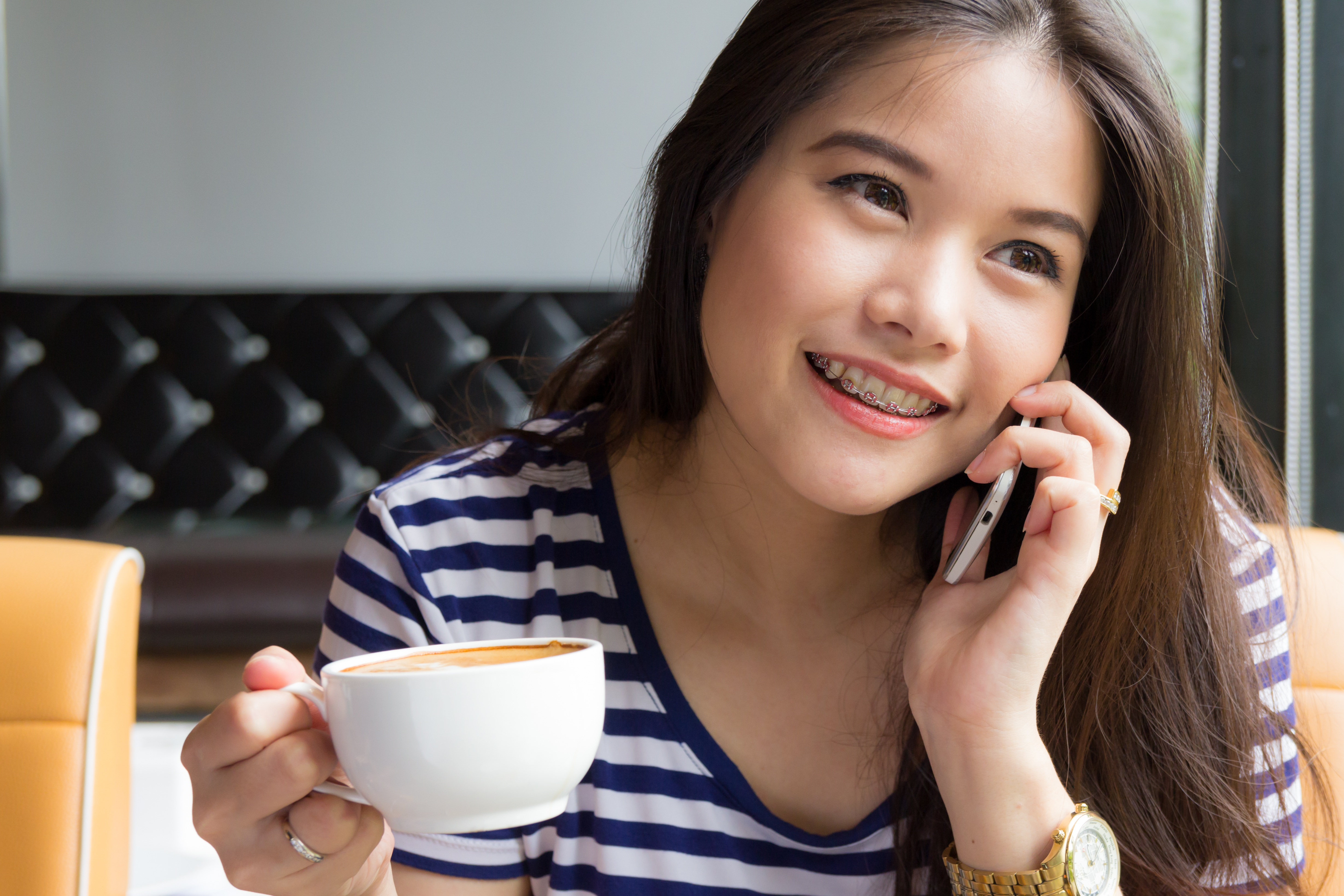 Young Asian woman with braces holds a cup of coffee and a phone.