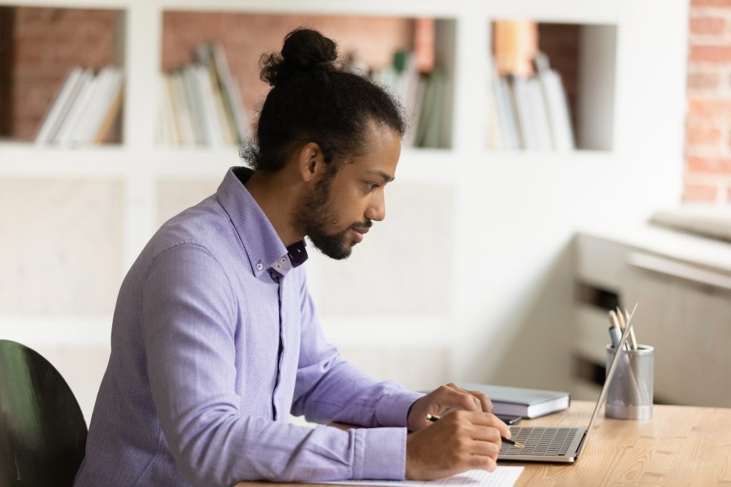 Young man completes an application while looking at a laptop computer.