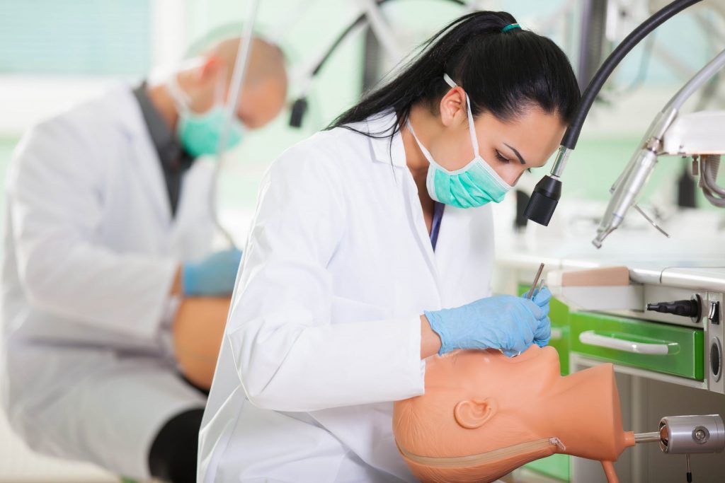 Students in lab coats studying to be dentists who specialize in treating gum disease practice technique on dummy heads.