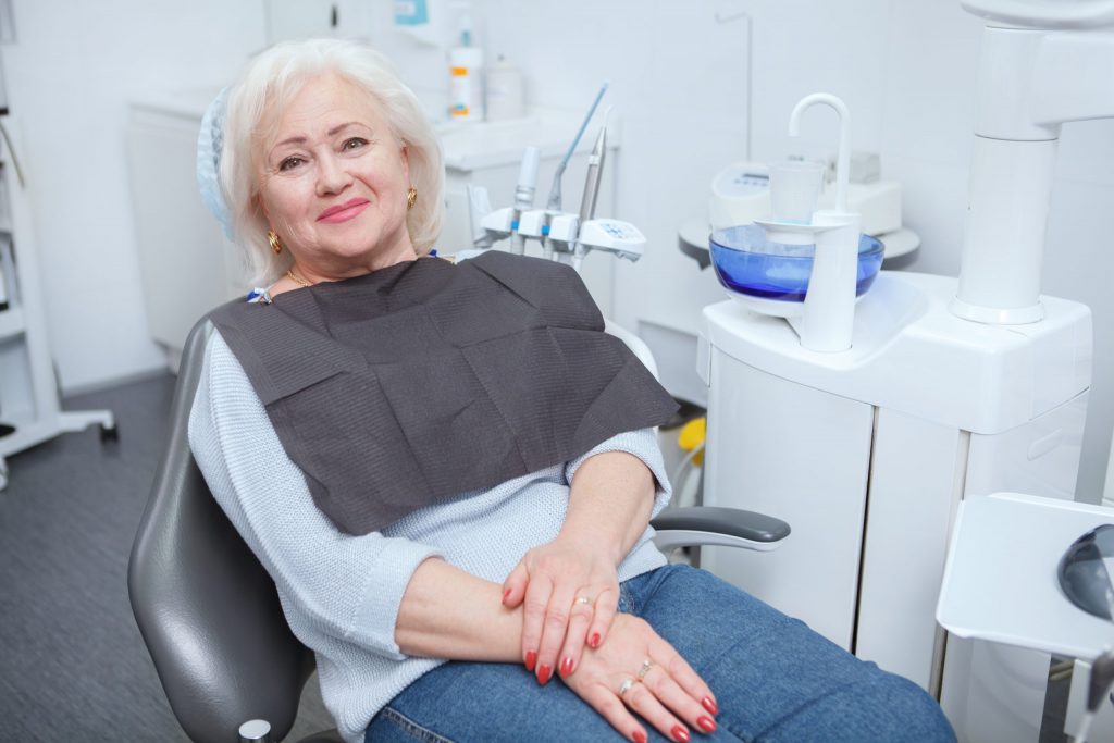  Woman wearing dental smock reclines in dental chair, awaiting professional cleaning of her teeth to maintain healthy gums. 