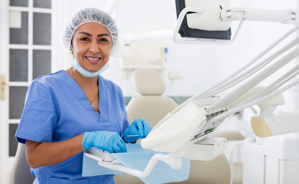 Smiling female dentist with PPE on preparing tray for a cleaning.