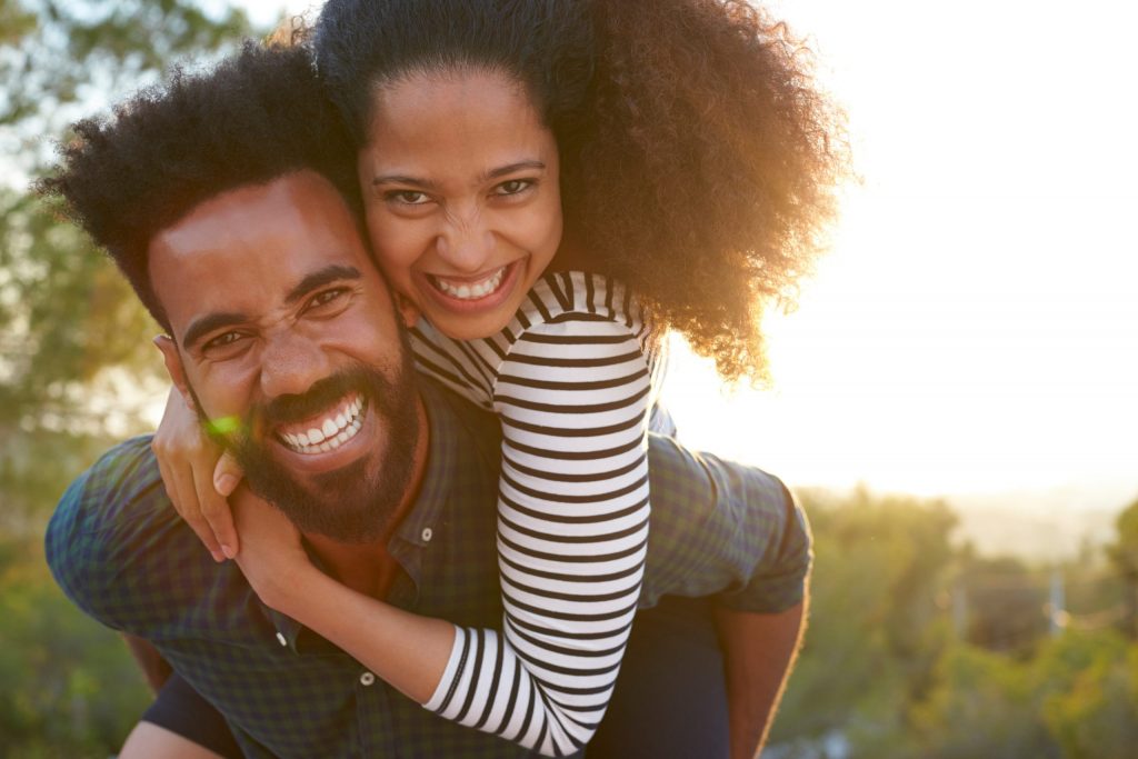 Man carrying young woman on his back while smiling outside.